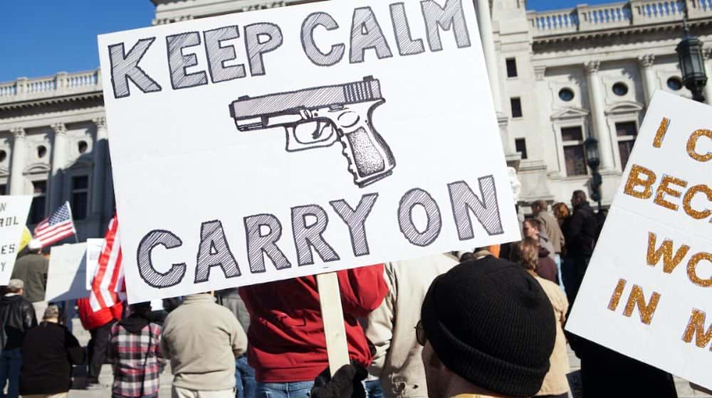 Protester holds keep calm carry on sign | Virginia Governor Bans Guns From State Capitol Ahead of Pro-Gun Rally | Featured