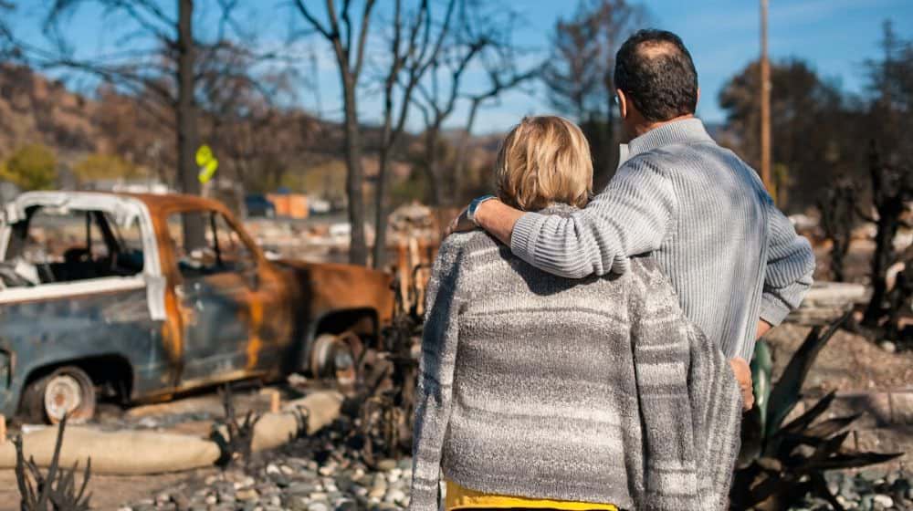 man and wife looking at their burned house | Natural Disasters: 5 Emergency Preparedness Tips for Seniors | Featured