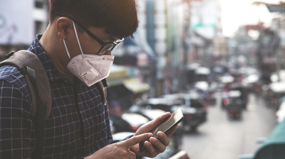 man with medical facemask using a mobile phone | Coronavirus to ‘Assume a Seasonal Nature’ If It Doesn’t Go ‘Globally Under Control,’ Dr. Anthony Fauci Claims | Featured
