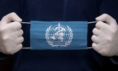 hand holding a mask with World Health Organization Logo | WHO Rejects ‘China-centric’ Charge After Trump Criticism | Featured