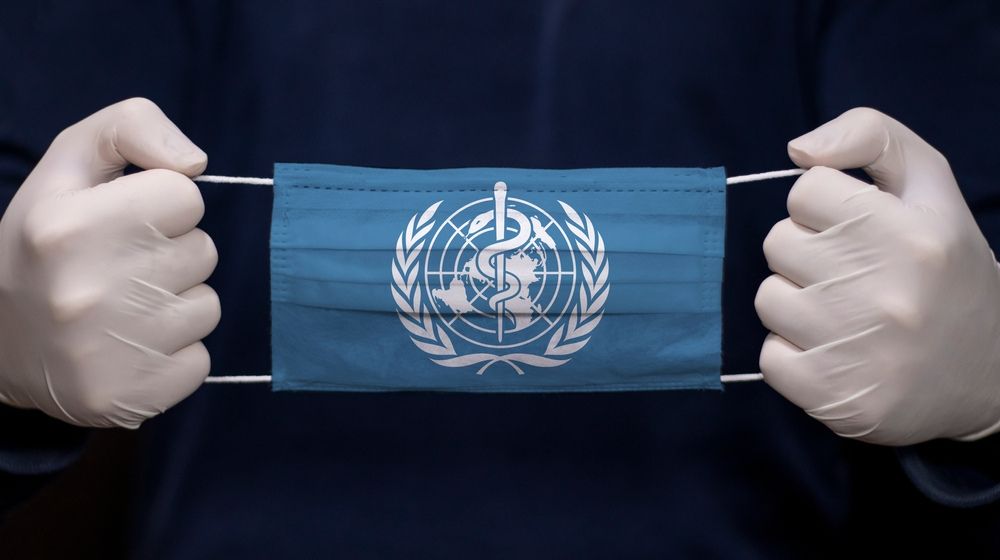 hand holding a mask with World Health Organization Logo | WHO Rejects ‘China-centric’ Charge After Trump Criticism | Featured