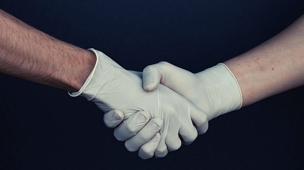 shaking hands with gloves | U.S. Records Lowest Number of COVID-19 Deaths in Two Weeks | Featured