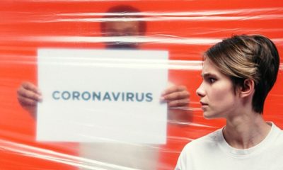 man holding paper with coronavirus behind the plastic cover and woman with worried face | WHO Clarifies That There Is “No Evidence” That Those Who Recovered from COVID-19 Are Safe from Reinfection | Featured