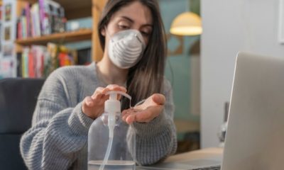 Business Woman Working from Home Wearing Protective Mask Cleaning Her Hands with Sanitizer | Majority of Americans Think Their Jobs Will Never Return to Normal | Featured