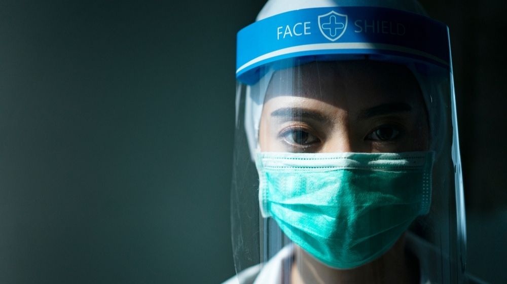 Closeup Asian Female Doctor Wearing Face Shield and PPE Suit | Fauci on COVID-19 Protection: “If You Have Goggles or an Eye Shield, You Should Use It” | Featured