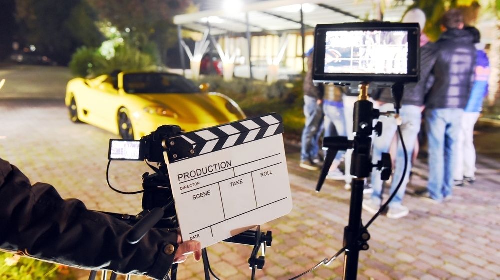 Operator Holding Clapperboard During the Production of Short Film Outdoor in the Night with Sportive Yellow Car | Movie Studios Must Undergo a Lot of COVID-19 Tests to Stay Secure and Open | Featured