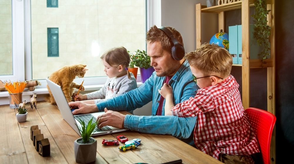 Man Works on Laptop with Children Playing Around | COVID-19 Pandemic Causes Americans to Struggle in Achieving Work-Life Balance | Featured