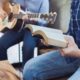 A Man Sing a Song from Hymn Book While His Friends Playing Guitar | California’s Ban on Singing in Churches Causes Outrage | Featured