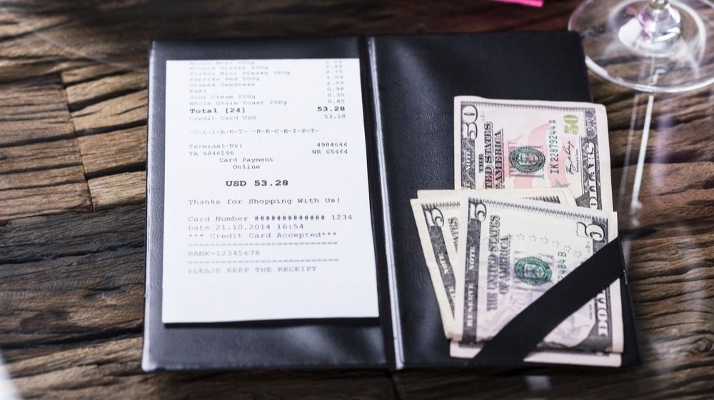 Elevated View Of Bill And Banknote On Wooden Desk | Restaurant Customers Do Not Like Being Forced to Tip Regardless Whether They Got Good or Bad Service | Featured