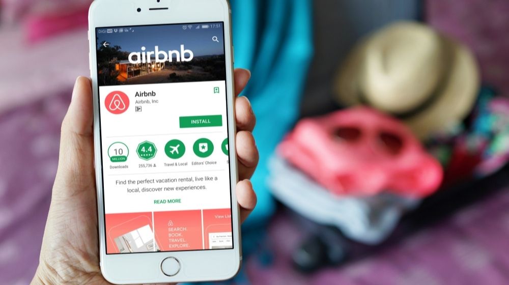 Female hand Holding Smartphone with Airbnb Application | Airbnb Launches New Pilot Restriction in the UK, France, and Spain to Reduce Unauthorized Parties | Featured