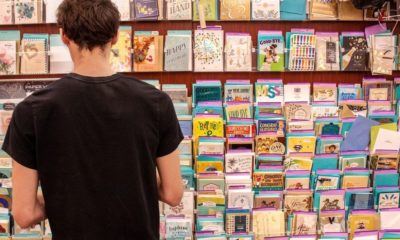 Man in Black Shirt Standing in Front of Greeting Cards Section of a Grocery Store | Greeting Card Company Hires Team of Employees Who Have Gone Through Homelessness to Design Its Cards | Featured