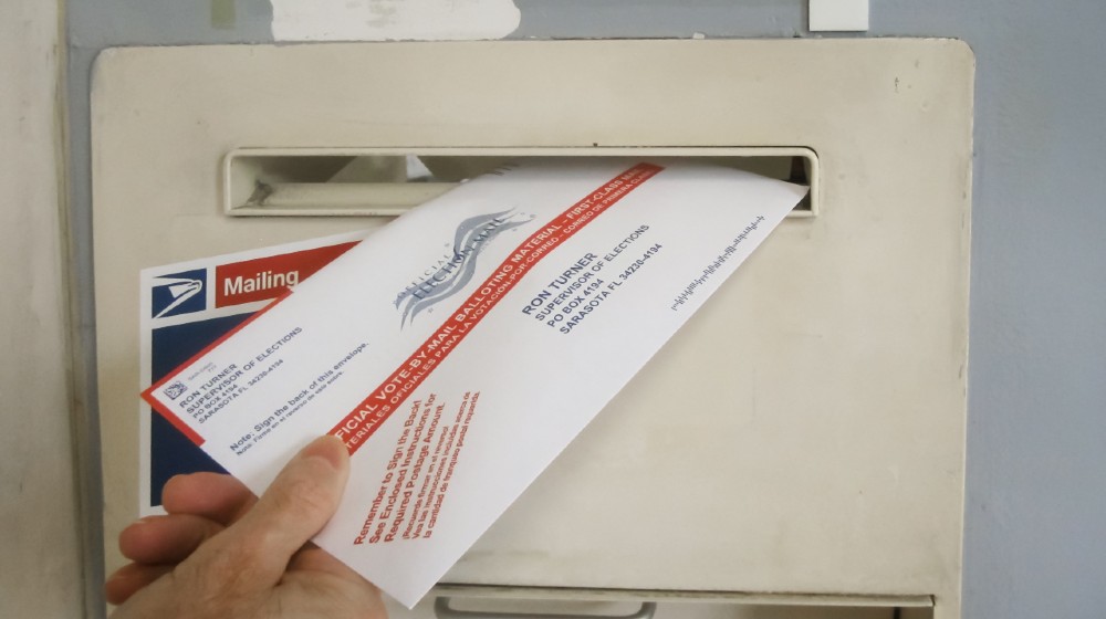 Absentee voter mailing vote by mail ballot at a U.S. Post Office mailbox-Uncounted Votes in Georgia-ss-featured
