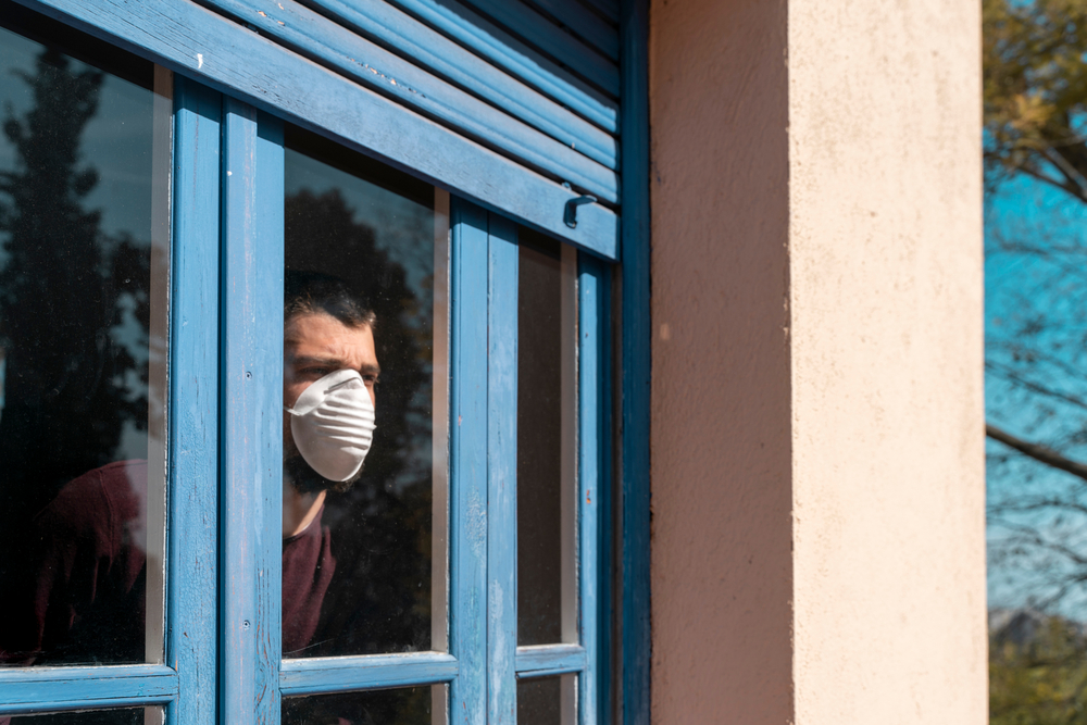 Man with mask in quarantine, looking outide the window-Governors Reinstate Severe Lockdowns as COVID-19 Cases Increase-ss-featured