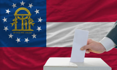 Person casting ballo tinto box with the Georgia state flag in the background- Georgia Begins Hand Recount; Expected to Be Completed By Wednesday-ss-featured