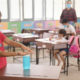 Three students and a teacher in a classroom with face mask and a girl applying hand sanitizer to her hands-Teachers’ Unions Call to Halt In-Person Learning as COVID-19 Cases Rise-ss-featured