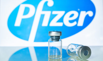 Vaccine vials in front of the Pfizer logo- Pfizer Coronavirus Vaccine Volunteer Talks About Its Side Effects-ss-Featured