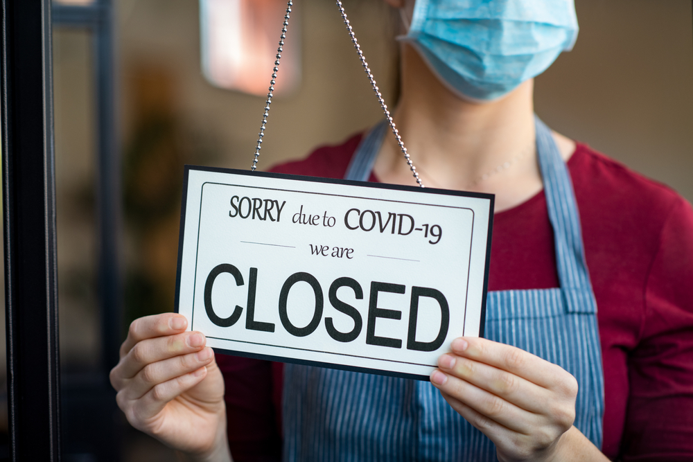 Woman with mask putting up store's "closed" sign due to COVID-19 lockdown-More Governors Issue Severe Coronavirus Restrictions as Cases Continue to Increase-ss-featured
