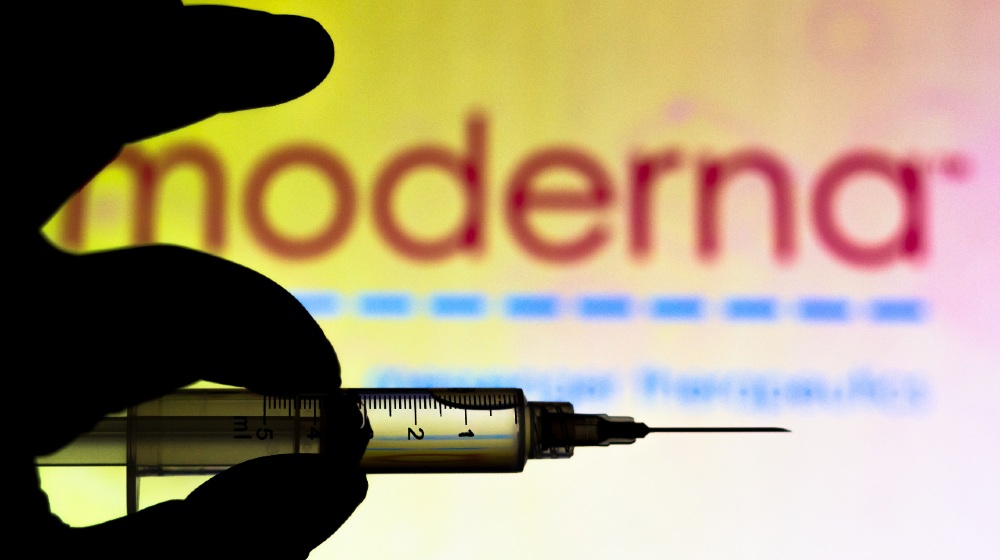 the-medical-syringe-coronavirus-vaccine-is-seen-with-Moderna-Therapeutics-company-logo-displayed-on-a-screen-in-the-background-Coronavirus-Vaccine-News-ss-featured