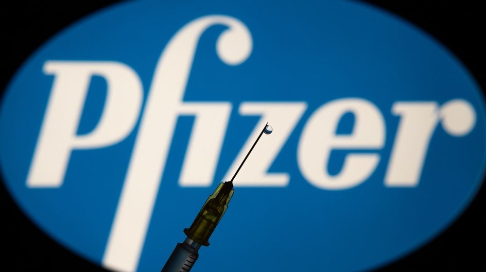 medical syringe in front of Pfizer Logo-U.S. Rolls Out First Doses Of Pfizer's COVID-19 Vaccine-ss-featured
