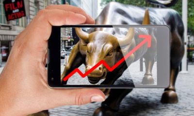 Hand pointing smartphone screen at bull of wall street in New York showing growing stock chart-Wall Street Record Highs-ss-featured