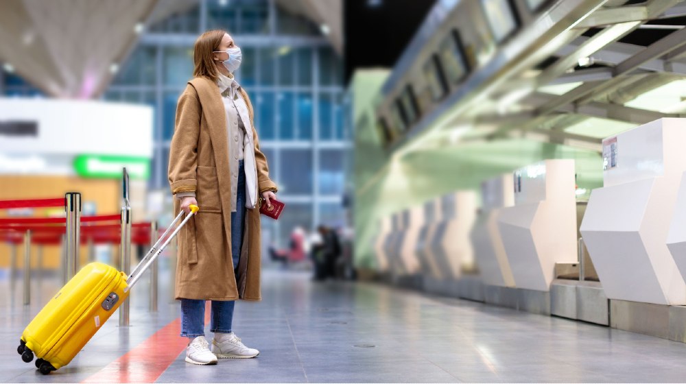 Woman with luggage stands at almost empty check-in counters at the airport terminal due to coronavirus pandemicCovid-19 outbreak travel restrictions-Requiring COVID Tests-ss-featured