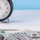 A table clock, stimulus check, and 100 dollar bills-Tax Return Timing Could Affect Your Stimulus Payout-ss-Featured