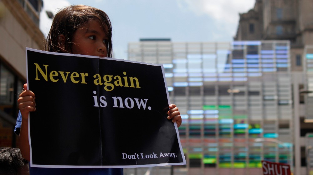 A young girl holds up a protest sign to demand the closure of detention camps at the U.S.-Mexico border-Border Detention Centers-ss-featured