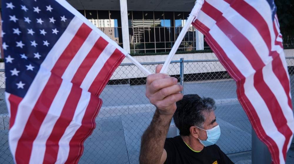 An immigration activist holding US flags- Lawmakers Warn Biden on Immigration Order Will Cause Crisis Overnight-ss-Featured