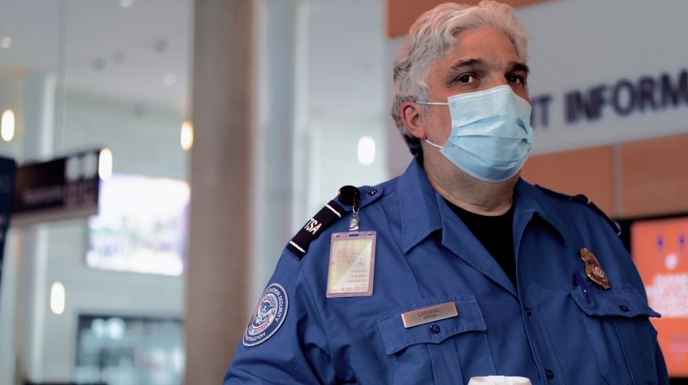 TSA agent wearing a facemask-TSA Will Require Travelers to Wear Facemask in Airports and Planes-ss-Featured