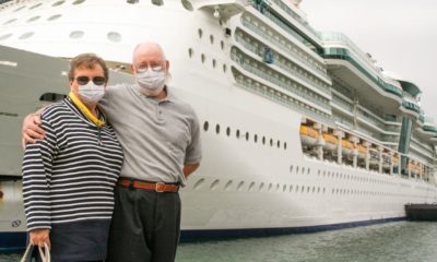 Senior Couple Wearing Face Masks Standing In Front of Passenger Cruise Ship-Cruise Lines Stocks-ss-featured