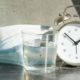glass of water, alarm clock and medical mask on a gray background-Covid Time Capsule-SS-Featured