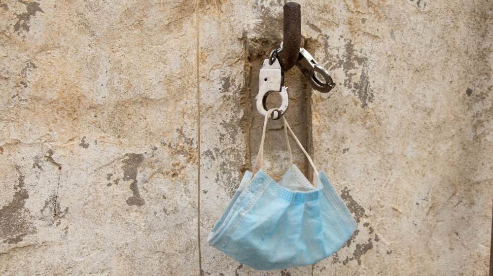 medical mask and handcuffs hang on a stone wall on a hook-Fraud-SS-Featured