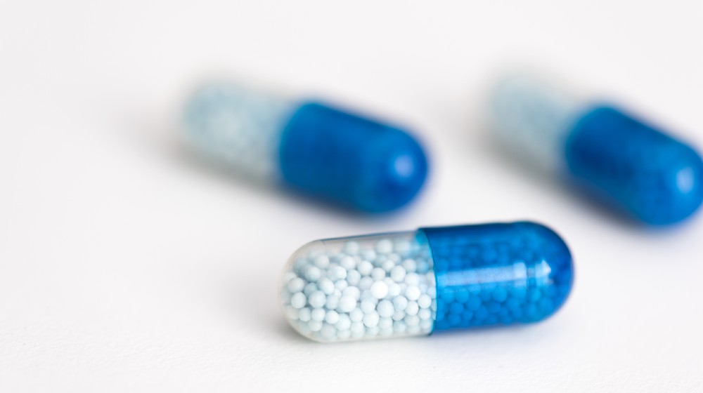 Blue capsule, pills on white background. Health care, medical, pharmacy concept | Pfizer Says COVID At-Home Pill Might Be Ready By Year End | Featured