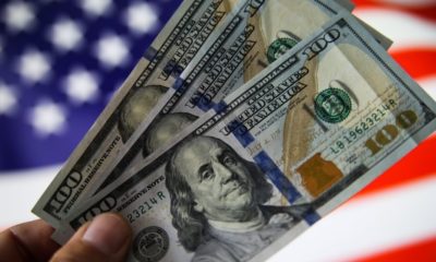 Hand holding hundred dollar bills with US flag in the background-'Put American Families First' House GOP wants Review of NY's $2B Relief for Illegal Immigrants-s-Featured