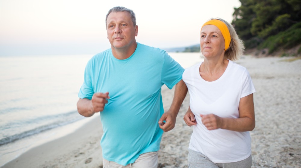 Senior couple jogging on the coast | Regular Exercise Helps COVID-19 Patients Avoid Hospitals | Featured