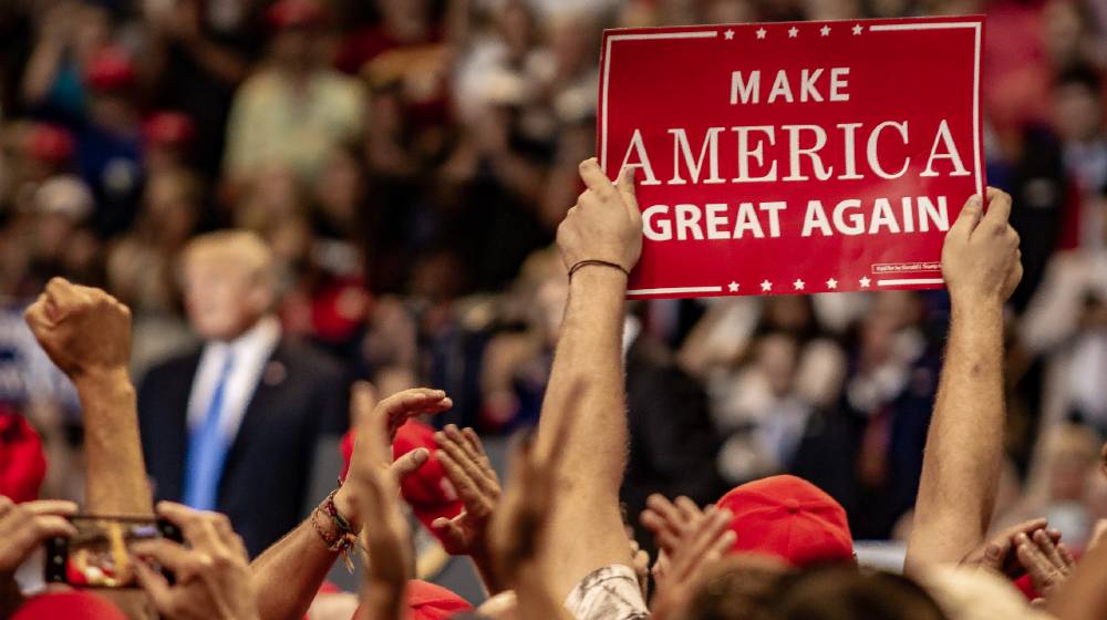 A fan holds up a Make America Great Again sign while President Donald J. Trump delivers a speech | Trump Alabama Rally Cancelled Due To Partisan Politics | featured