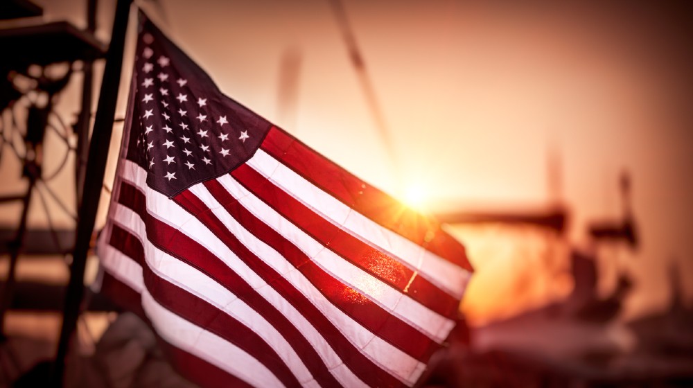 Flag of United States of America flutters in the winds in mild sunset light | 5 Priorities For America To Address | featured