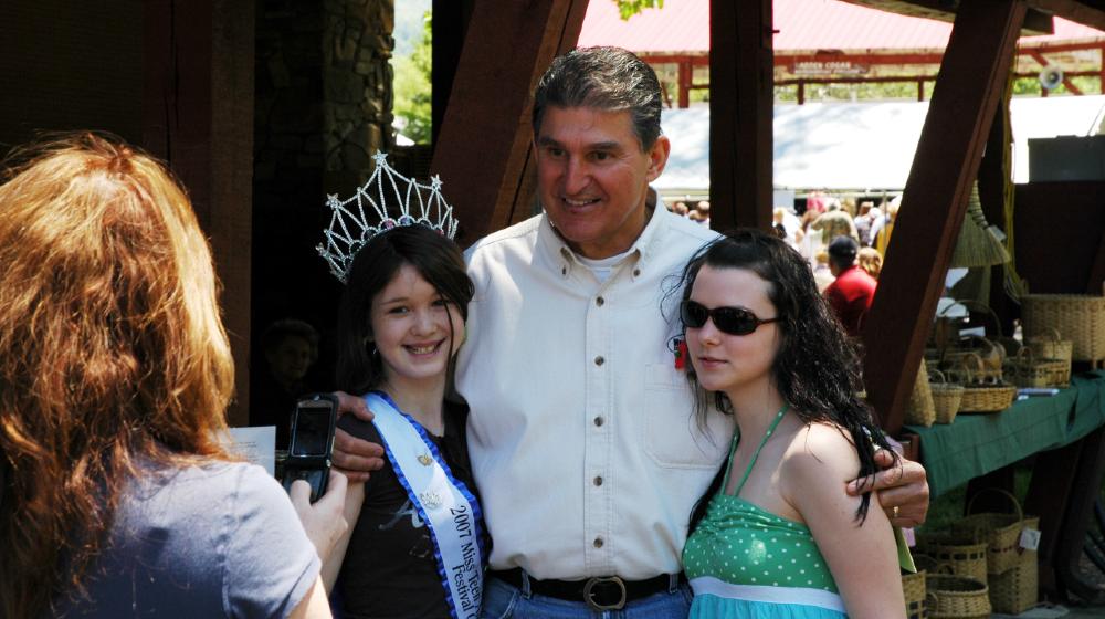 Governor Joe Manchin poses for cell phone photo with a local beauty queen and her friend during the Webster County Woodchopping Festival | Manchin Won’t Support Democrats’ Voting Rights Bill | featured
