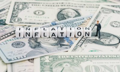 Miniature people businessman standing and wise thinking with cube block combine word Inflation on US dollar money banknote | Inflation Explained | featured