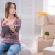 Neat and organized. Pleasant young woman sitting on the pouf in her old apartment and checking the list of items in the notebook before moving out | Important Facts About Moving Insurance | featured