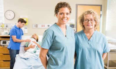 Portrait of confident nurses standing against couple with newborn baby at hospital
