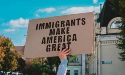 The phrase Immigrants Make America Great on a carton banner in men's hand | Case Against Immigration Activist Maru Mora Villalpando | featured
