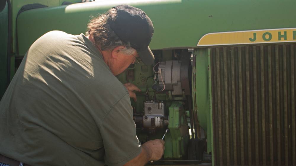 Cultural Equipment Mechanic working on an antique John Deere tractor | John Deere Workers Stage Walkout Then Went On Strike | featured