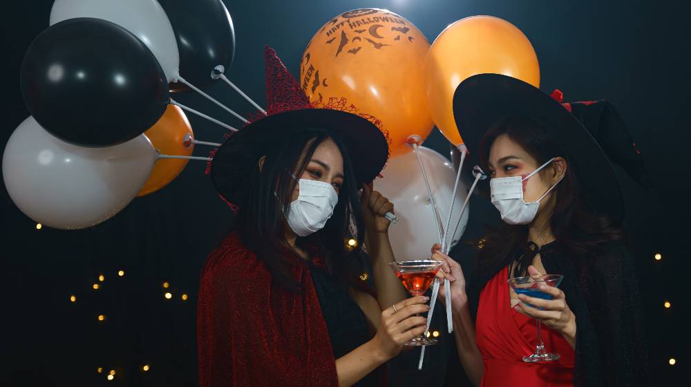 portrait of two asian women in witches costume wearing protective face mask to protect coronavirus covid-19 | How To Have a Lockdown Halloween Party | featured