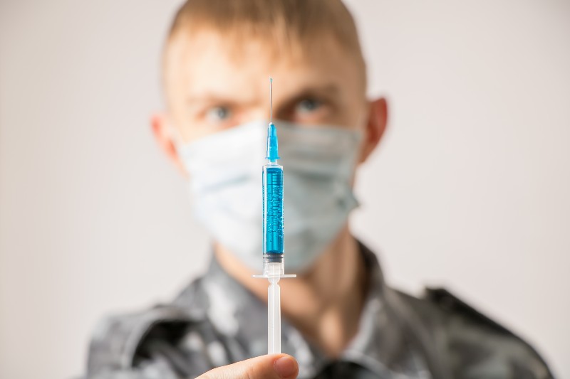 A military medic or doctor in a medical protective mask holds a syringe-Oklahoma National Guard