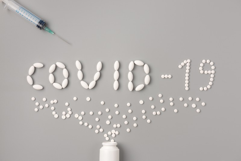 Flat lay of medicine pills shape as word covid 19 with syringe-COVID Pill