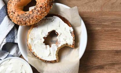 A bagel with cream cheese on a plate and a bite taken out | Kraft’s Cream Cheese Shortage Can Win Some Americans $20 | featured