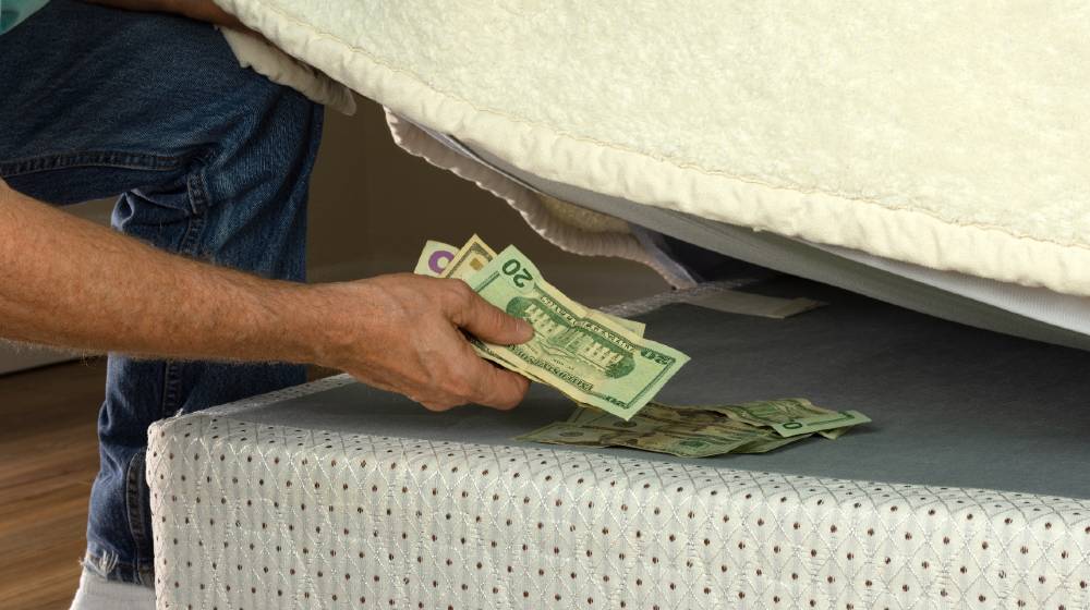 Man putting money under his mattress to save it showing no trust in financial institutions and banks | 8 Simple Ways To Save Money | featured
