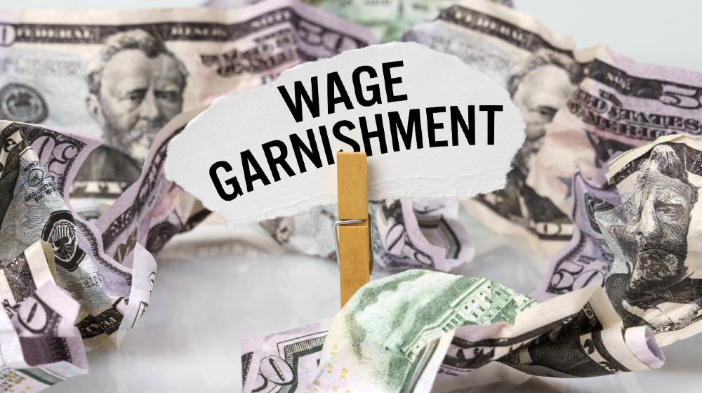 There are dollars on the table and there is a clothespin with paper on which it is written - WAGE GARNISHMENT | How to Make a Payment Arrangement to Stop Wage Garnishment | featured
