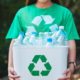 A woman collecting garbage and holding a recycle bin with plastic bottles in the outdoors | Global Plastic Recycling: Fixing a Broken System | featured